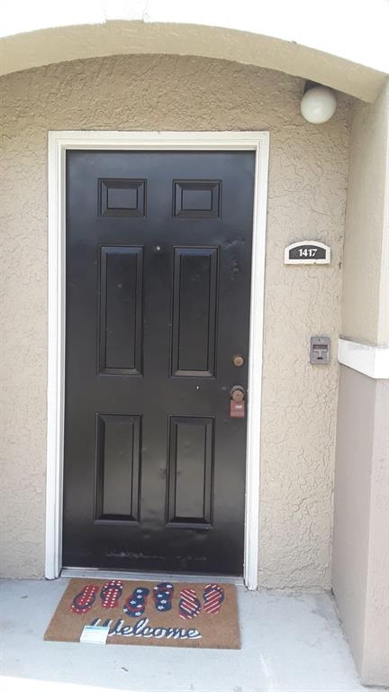 A black front door with a welcome mat sits under an arched entryway — 6512 SWISSCO DRIVE UNIT 1417, ORLANDO, FL