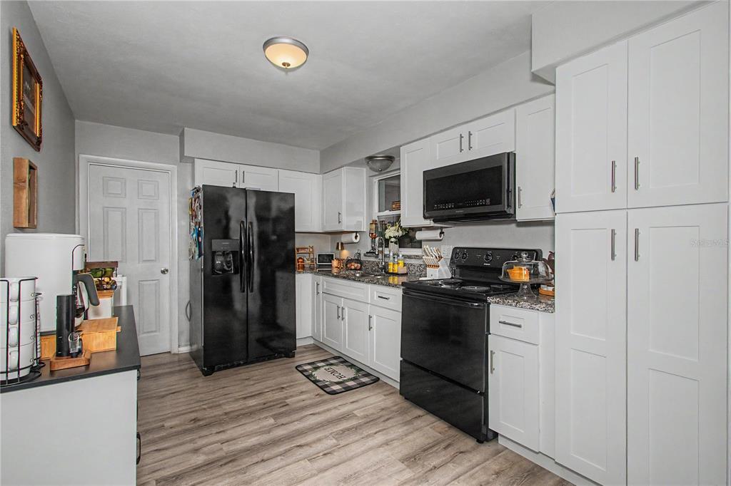 A kitchen features white cabinetry, black appliances, granite countertops, and light wood-look flooring — 20260 SW 80TH PLACE ROAD, DUNNELLON, FL