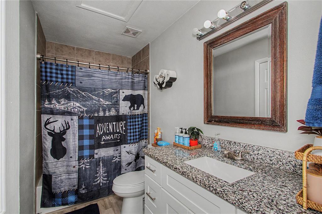 A bathroom features a granite vanity, a rustic wood-framed mirror, and a woodland-themed shower curtain — 20260 SW 80TH PLACE ROAD, DUNNELLON, FL