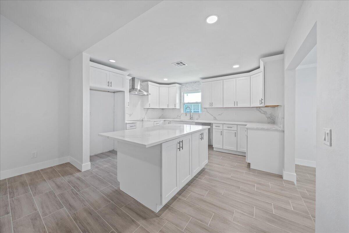 A modern kitchen features white cabinets, a central island, and light wood-look tile flooring — 179 Filbert Street, Sebastian FL 32958, SEBASTIAN, FL