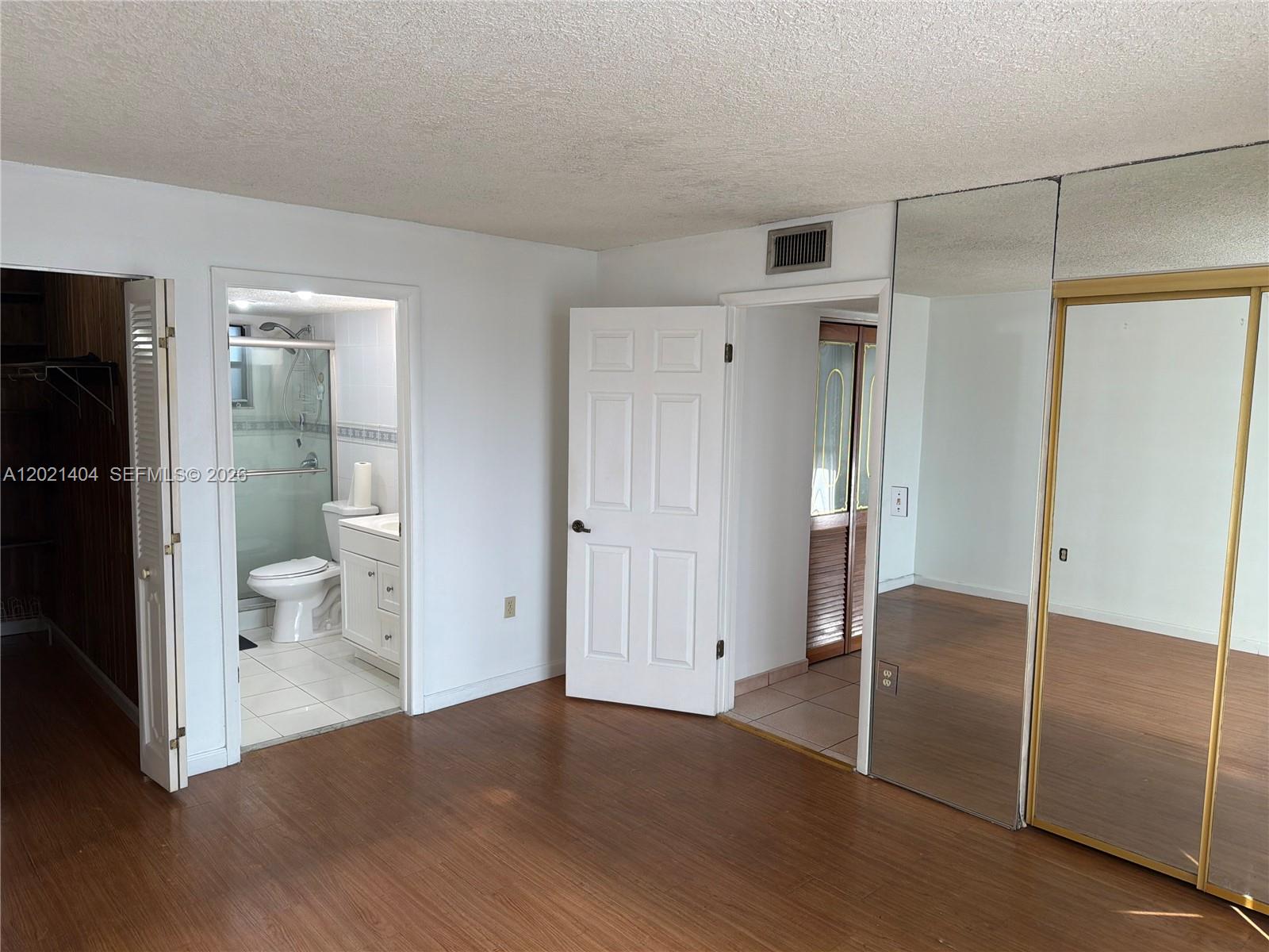 A bedroom with wood-look flooring, a mirrored closet, and an attached bathroom — 7300 Wayne Ave # 514, Miami Beach FL 33141, MIAMI BEACH, FL