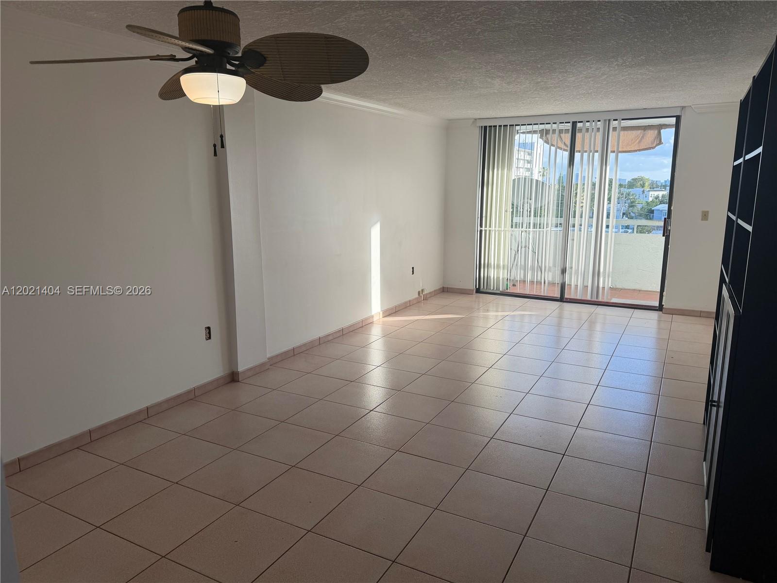 An empty room features light-colored tile flooring, a ceiling fan, and a sliding glass door — 7300 Wayne Ave # 514, Miami Beach FL 33141, MIAMI BEACH, FL