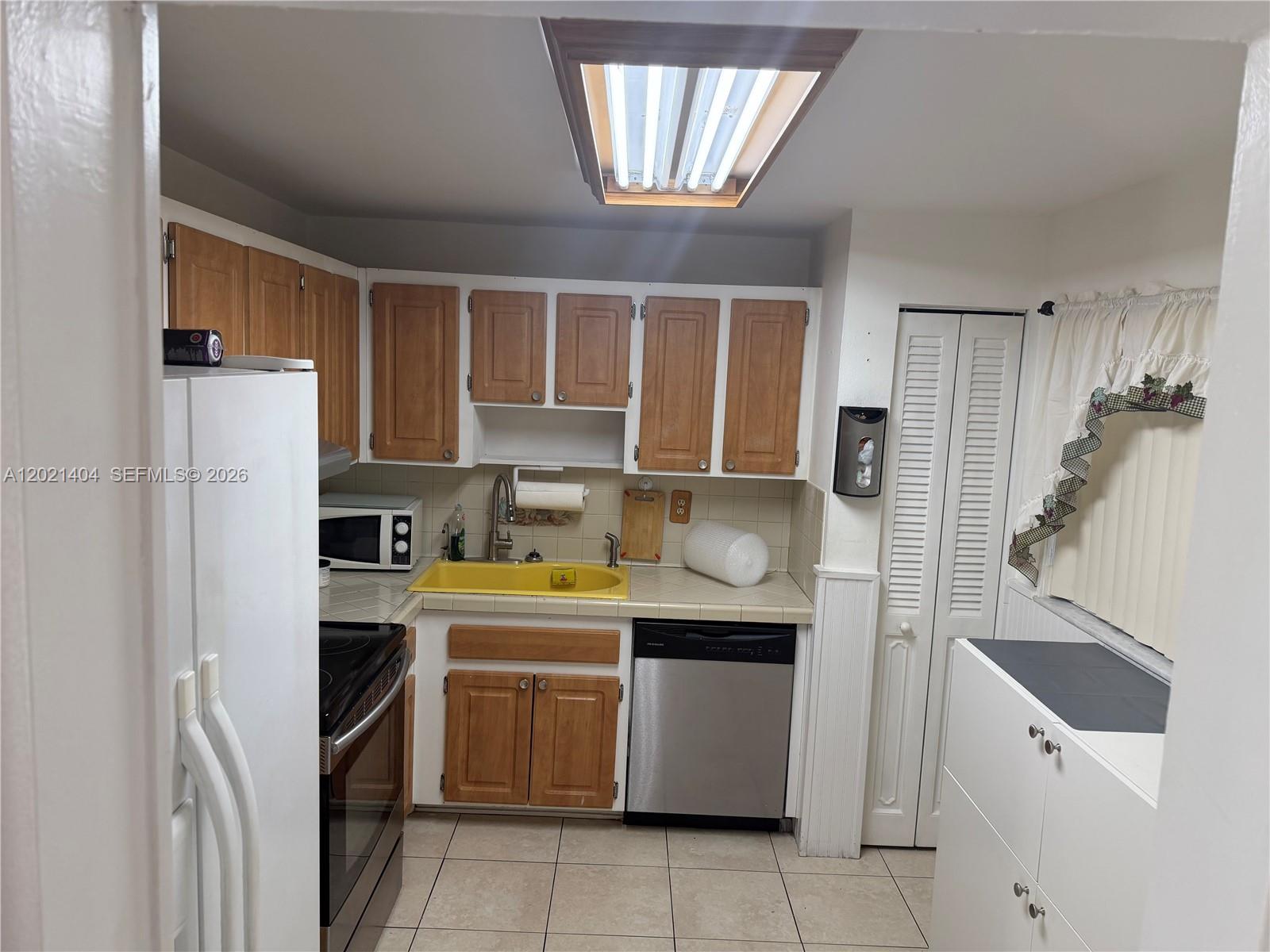 A kitchen features wood cabinets, a yellow sink, stainless steel dishwasher, and white appliances — 7300 Wayne Ave # 514, Miami Beach FL 33141, MIAMI BEACH, FL