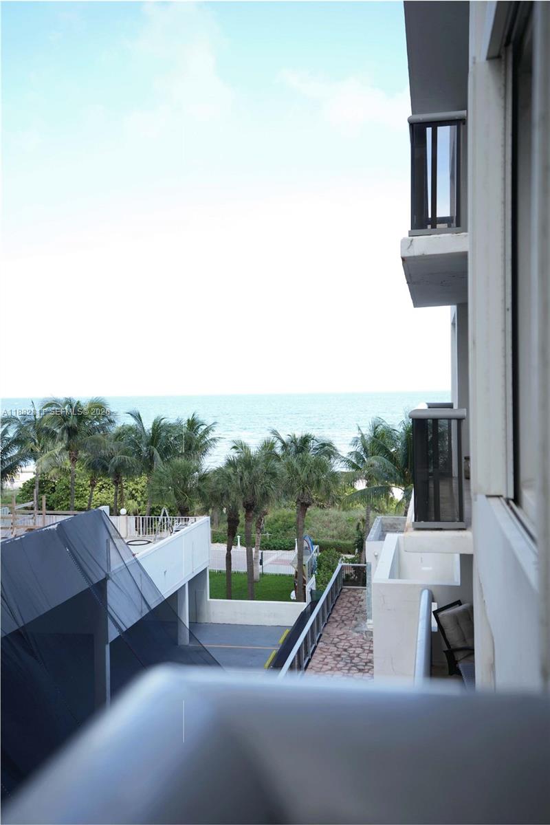 A view from a balcony overlooking palm trees, a parking area, and the ocean — 6039 Collins Ave # 503, Miami Beach FL 33140, MIAMI BEACH, FL