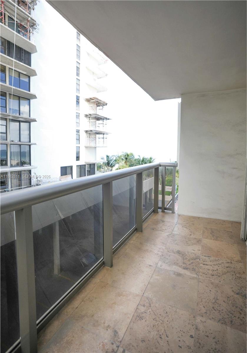 A balcony with stone tile flooring and a glass railing overlooks a neighboring building — 6039 Collins Ave # 503, Miami Beach FL 33140, MIAMI BEACH, FL