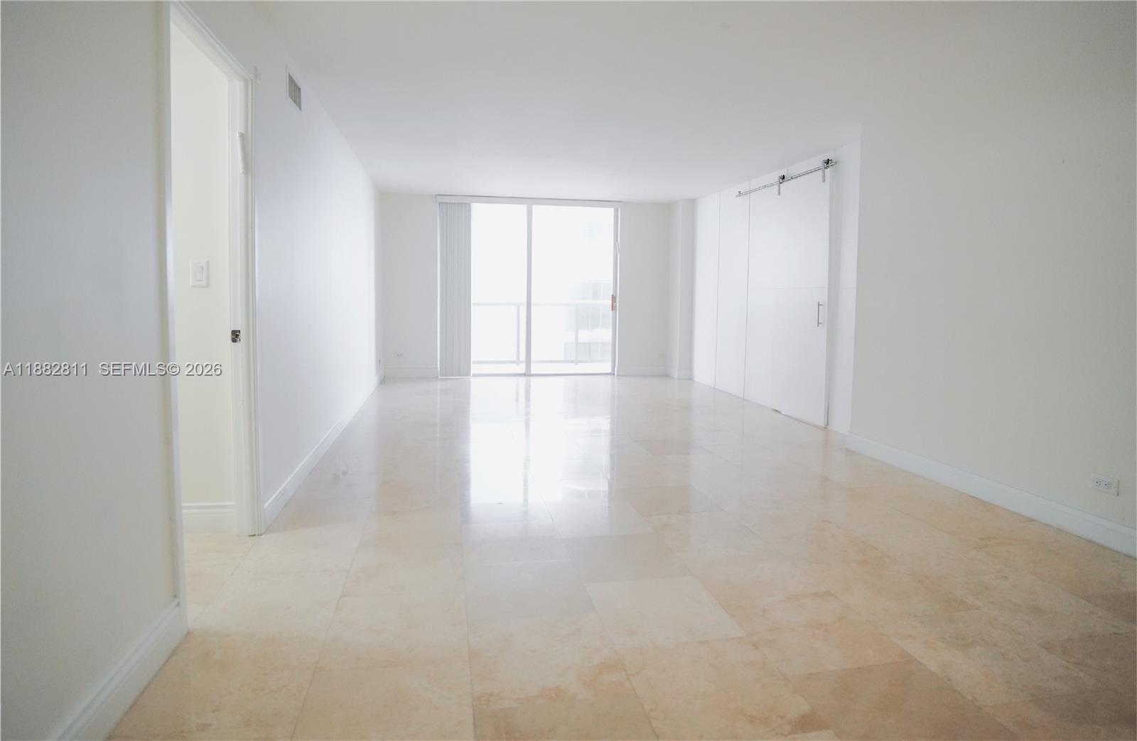 An empty room features white walls, light-colored tile flooring, and a sliding barn door — 6039 Collins Ave # 503, Miami Beach FL 33140, MIAMI BEACH, FL