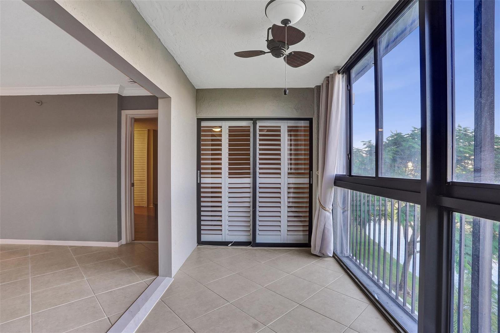 A tiled sunroom features a ceiling fan, sliding louvered doors, and large windows overlooking trees — 2334 S Cypress Bend Drive # 304, Pompano Beach FL 33069, POMPANO BEACH, FL
