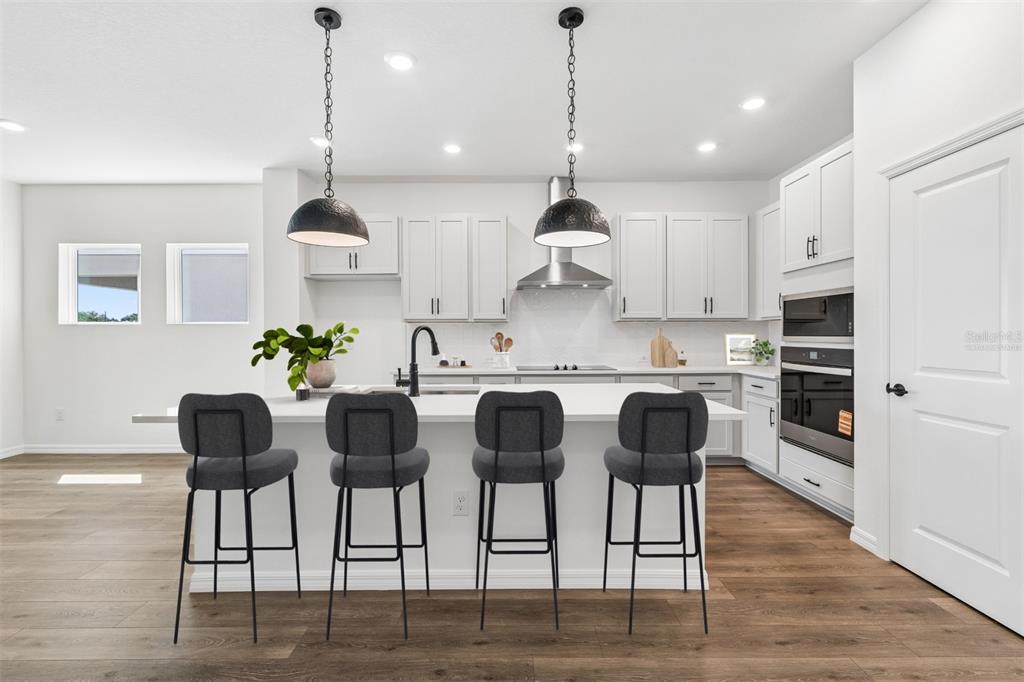 A modern kitchen features white cabinetry, a central island with four stools, and stainless appliances — 15231 EASTLYN DRIVE, BRADENTON, FL