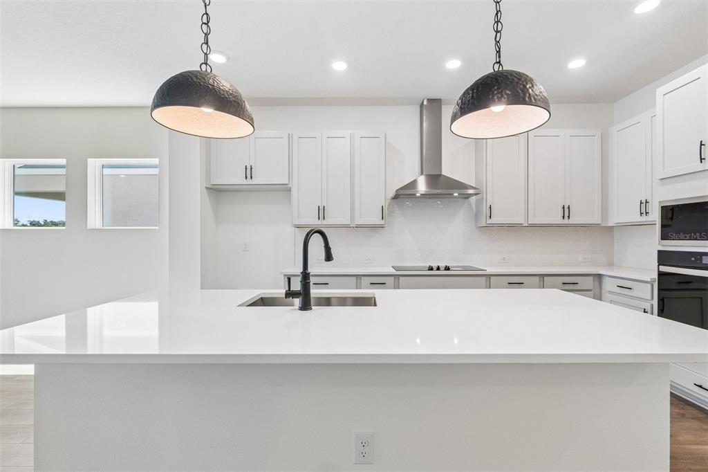 A modern kitchen features white cabinetry, a large island with a sink, and pendant lighting — 15231 EASTLYN DRIVE, BRADENTON, FL