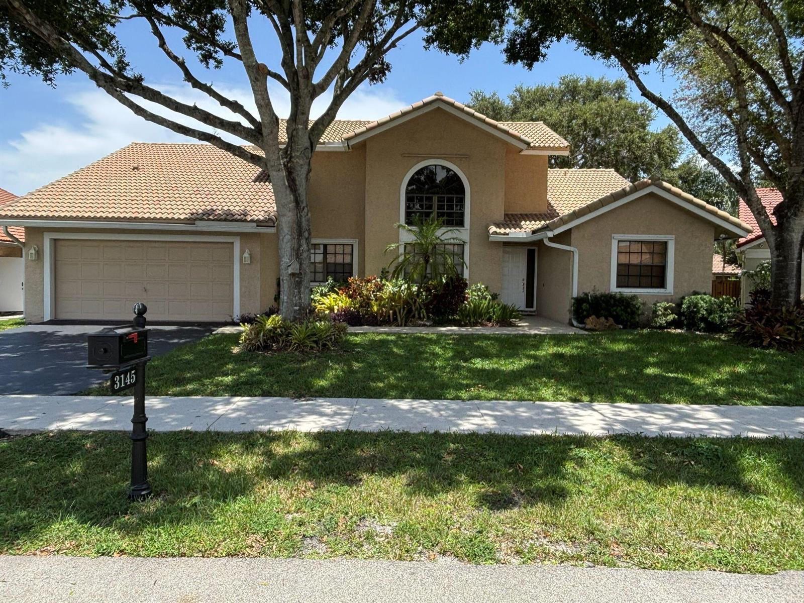 A paved driveway leads toward a brick entrance gate surrounded by trees and green lawn — 3145 Peachtree Way, Davie FL 33328, DAVIE, FL