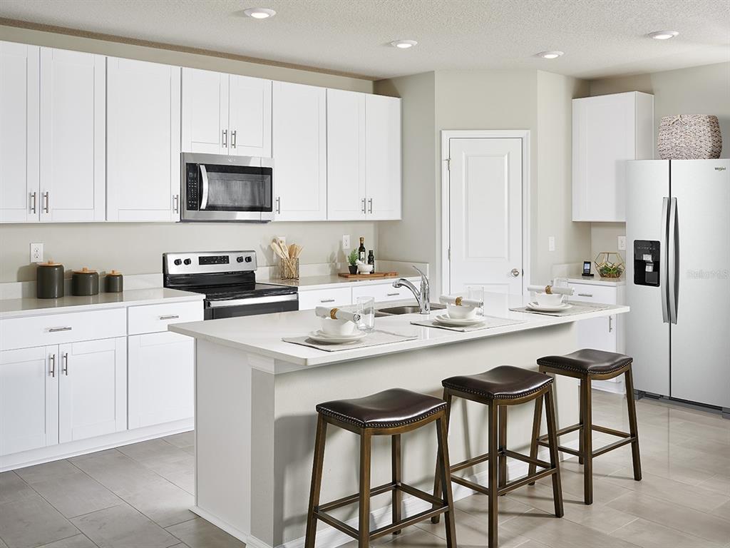 A modern kitchen features white cabinets, quartz countertops, a center island, and three bar stools — 145 ARCHER DRIVE, LAKE ALFRED, FL