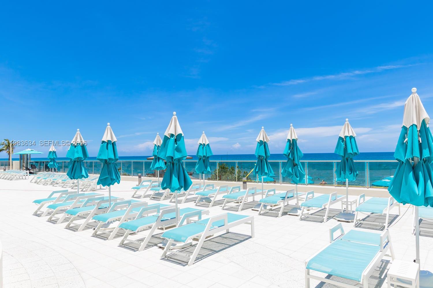 A pool deck features rows of lounge chairs and blue umbrellas overlooking the ocean — 2501 S OCEAN DR # 411, Hollywood FL 33019, HOLLYWOOD, FL