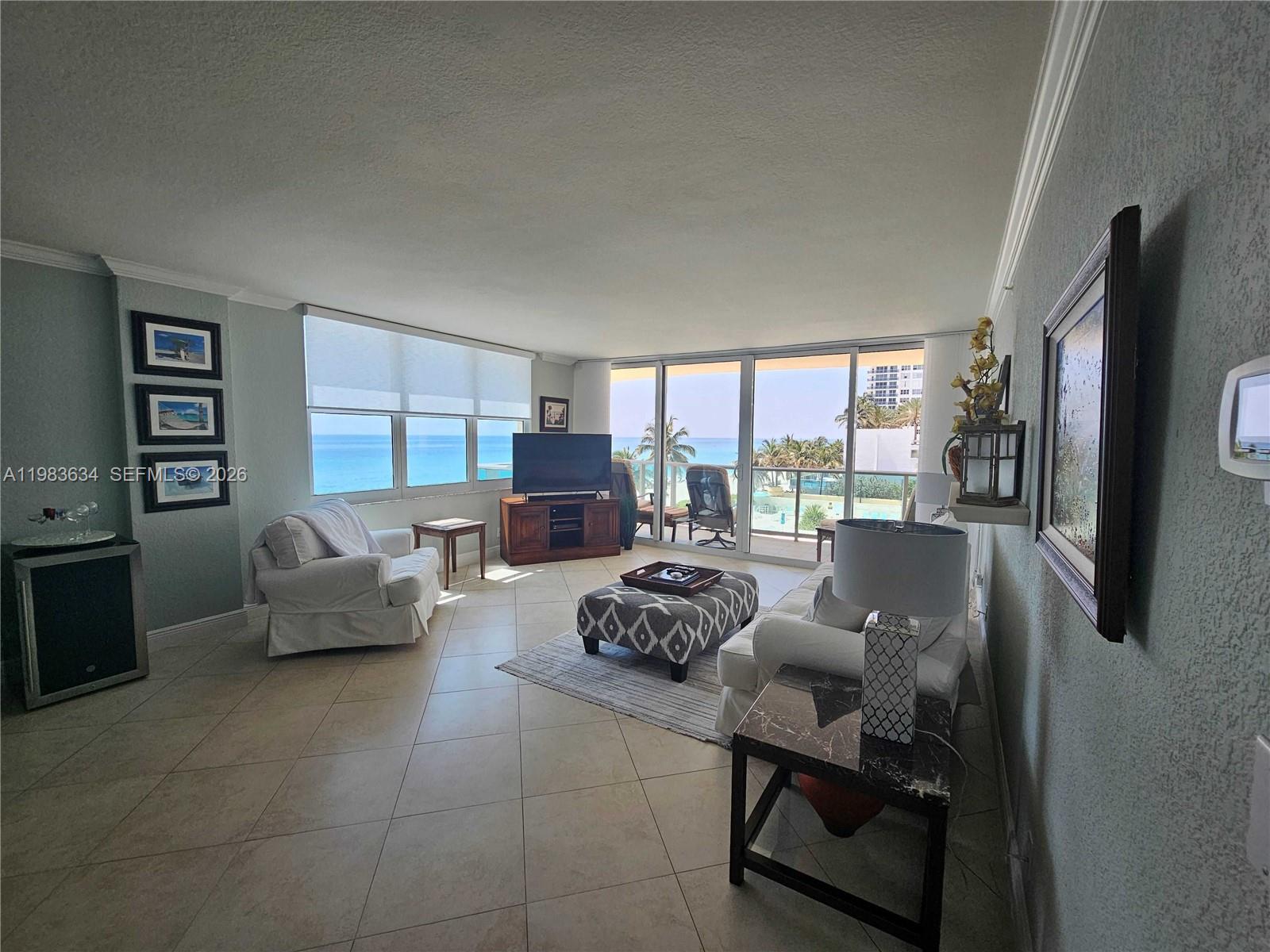 A living room features tile floors, a patterned ottoman, and floor-to-ceiling windows overlooking the ocean — 2501 S OCEAN DR # 411, Hollywood FL 33019, HOLLYWOOD, FL