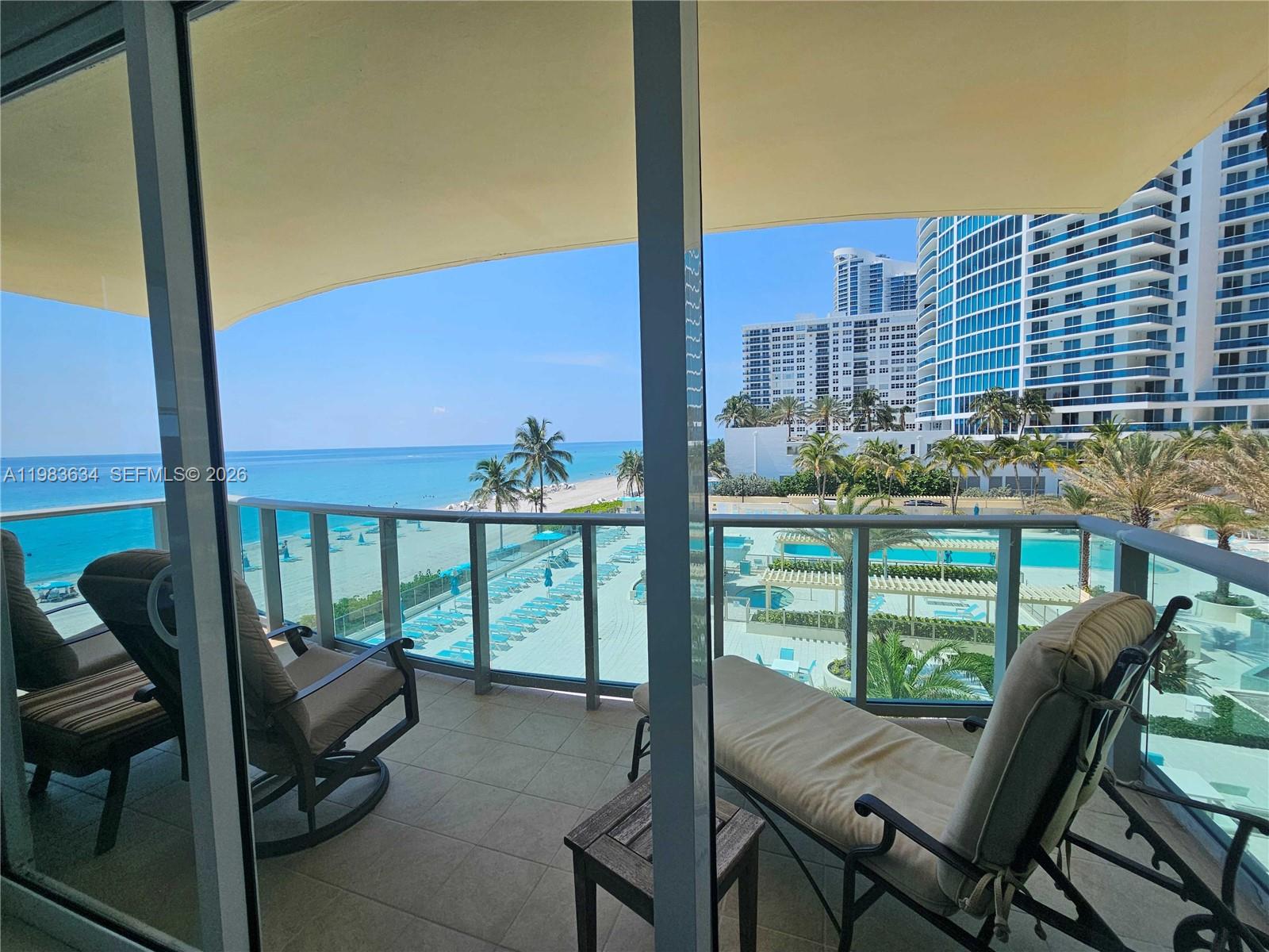 A balcony with lounge chairs overlooks a swimming pool, beach, and oceanfront high-rise buildings — 2501 S OCEAN DR # 411, Hollywood FL 33019, HOLLYWOOD, FL