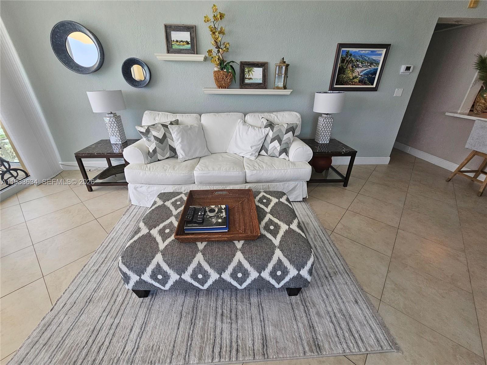 A living room features a white sofa, a patterned ottoman, and wall-mounted decor — 2501 S OCEAN DR # 411, Hollywood FL 33019, HOLLYWOOD, FL