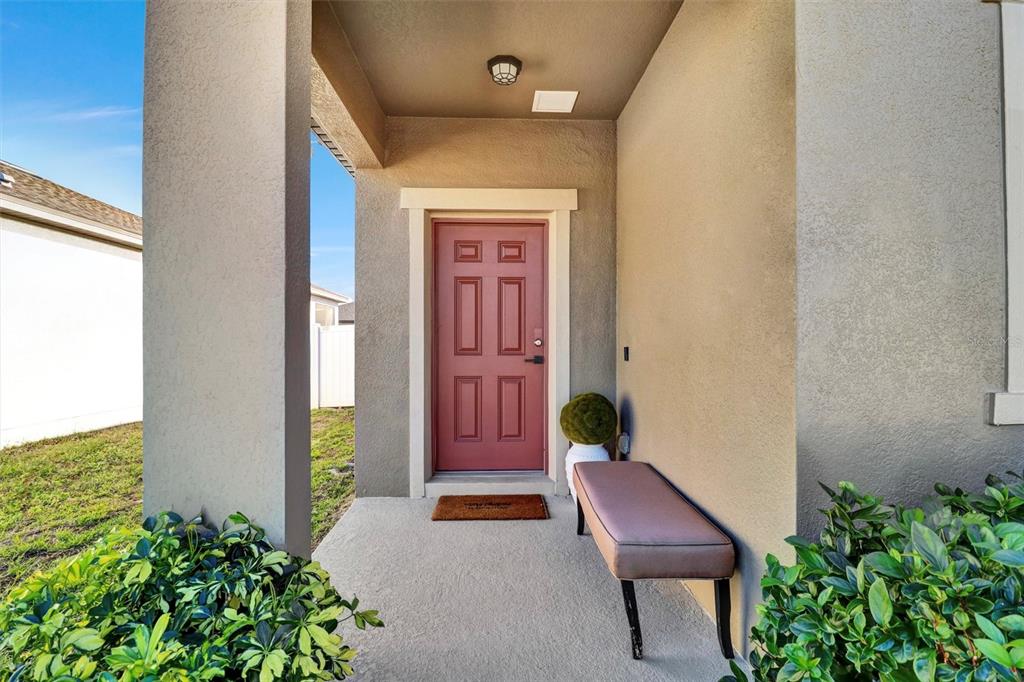 A covered entryway features a red front door, a small bench, and green landscaping — 5860 BOVINE DRIVE, ST CLOUD, FL