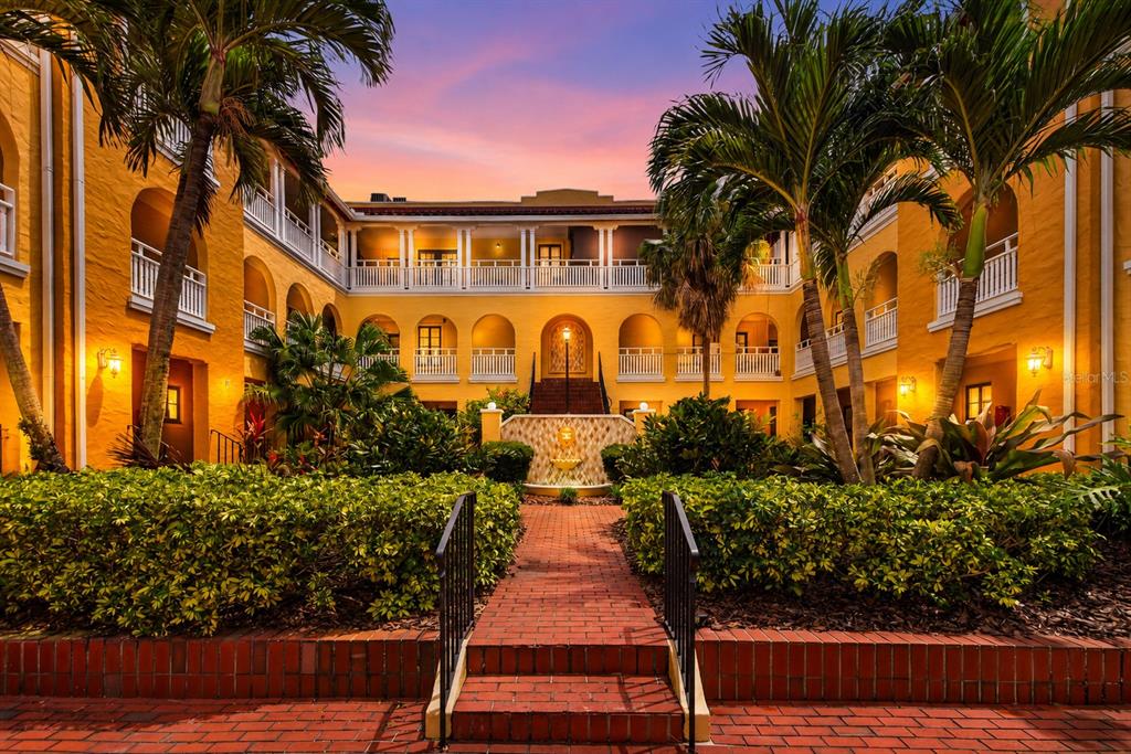 A courtyard with a brick walkway, fountain, landscaping, and palm trees at a yellow building — 210 22ND AVENUE NE UNIT 12, ST PETERSBURG, FL