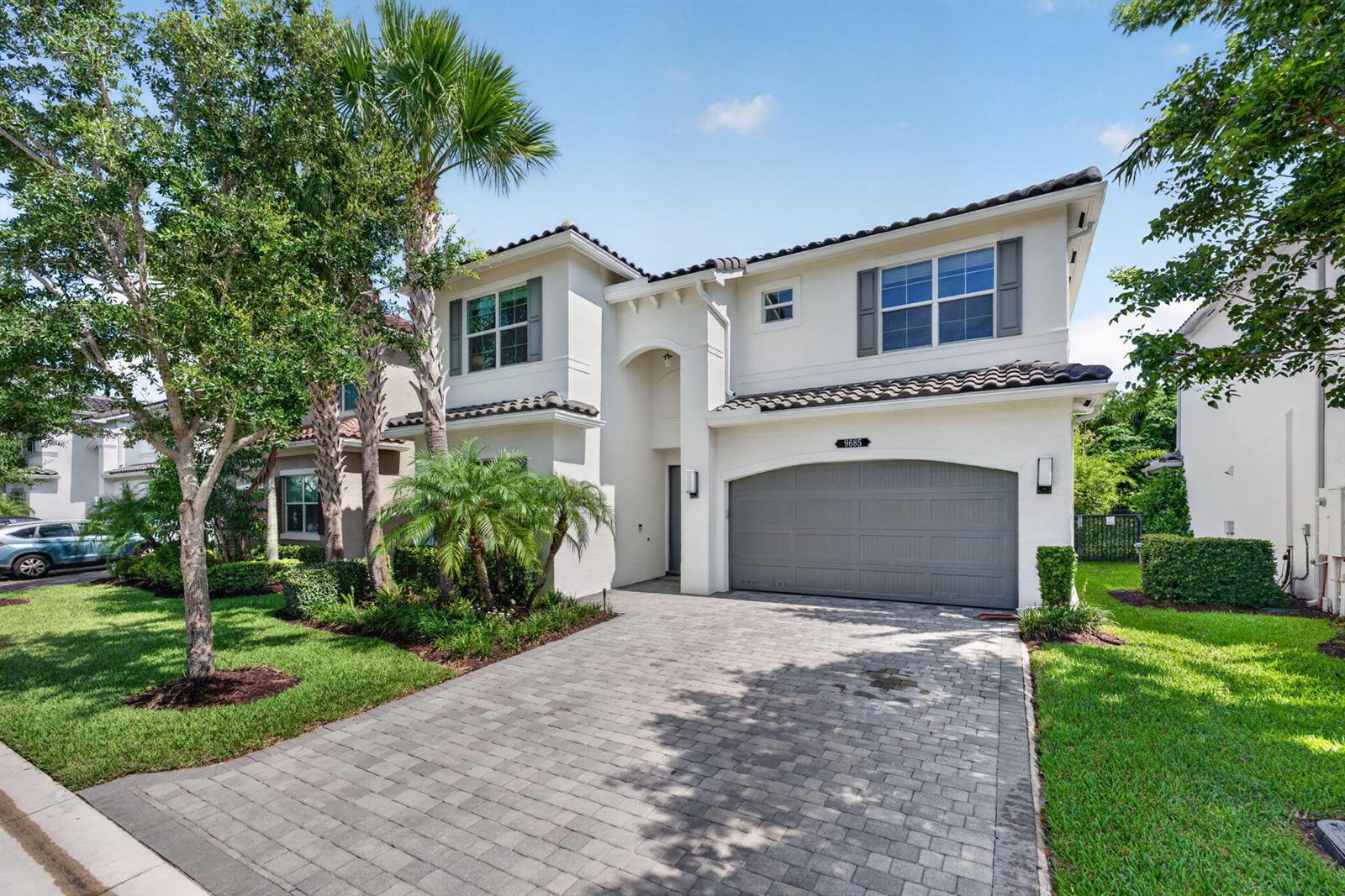A two-story stucco house features a gray garage door and a paved driveway — 9685 Salty Bay Drive, Delray Beach FL 33446, DELRAY BEACH, FL