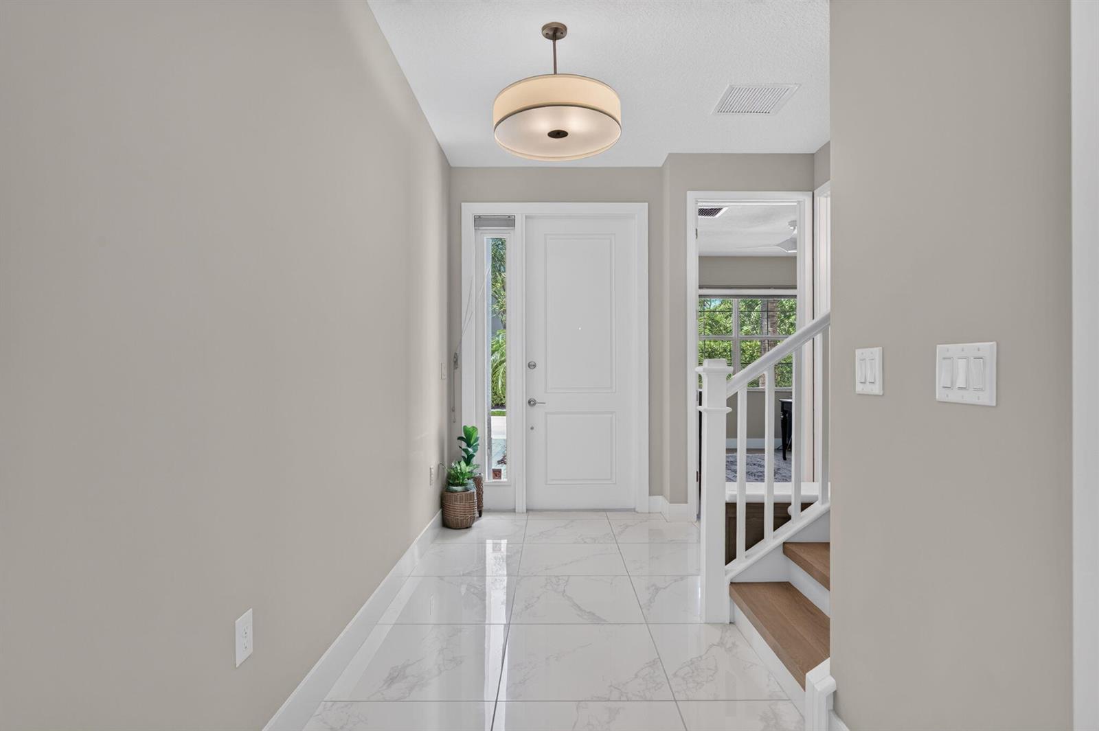 A bright entryway features white marble-look tile flooring, a modern drum light, and wooden stairs — 9685 Salty Bay Drive, Delray Beach FL 33446, DELRAY BEACH, FL