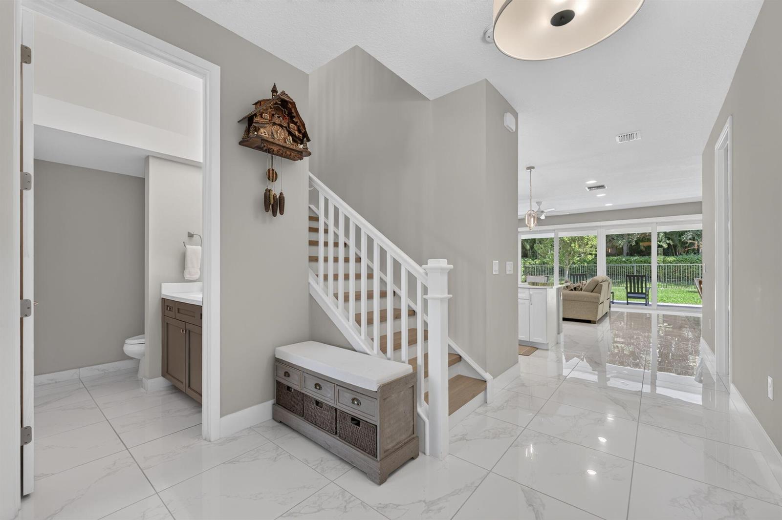 An entryway features a staircase, a wooden storage bench, and a view into the living area — 9685 Salty Bay Drive, Delray Beach FL 33446, DELRAY BEACH, FL