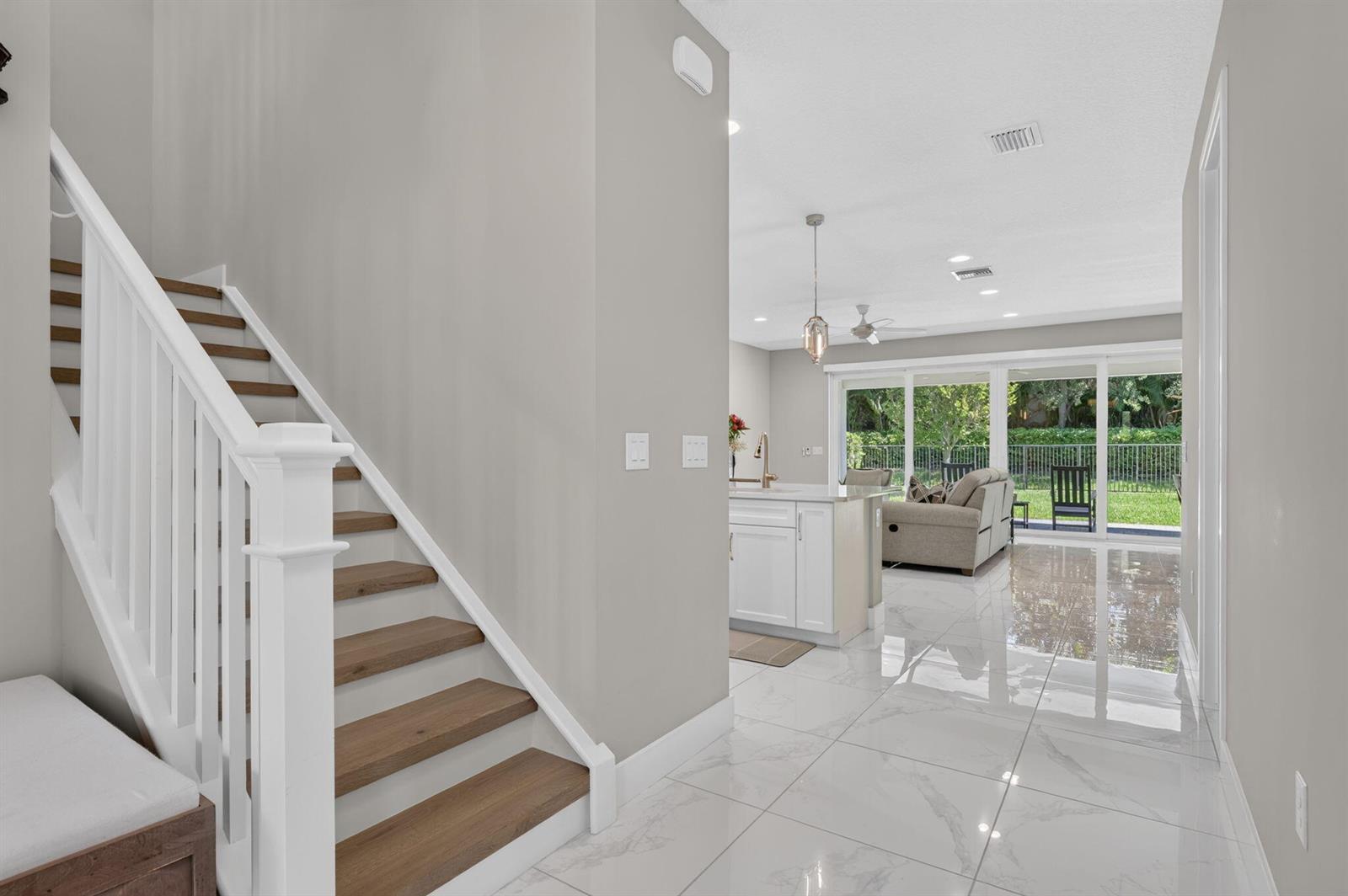 A staircase with wooden treads leads to an open-concept kitchen and living area with tile — 9685 Salty Bay Drive, Delray Beach FL 33446, DELRAY BEACH, FL