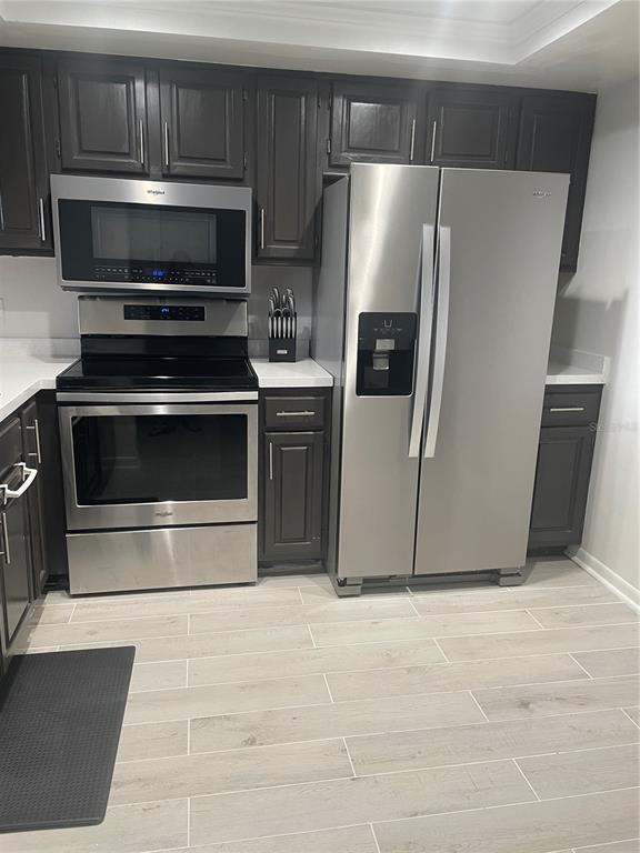 A kitchen features dark cabinets, stainless steel appliances, white countertops, and light wood-look tile flooring — 106 1ST STREET E UNIT 306, ST PETERSBURG, FL