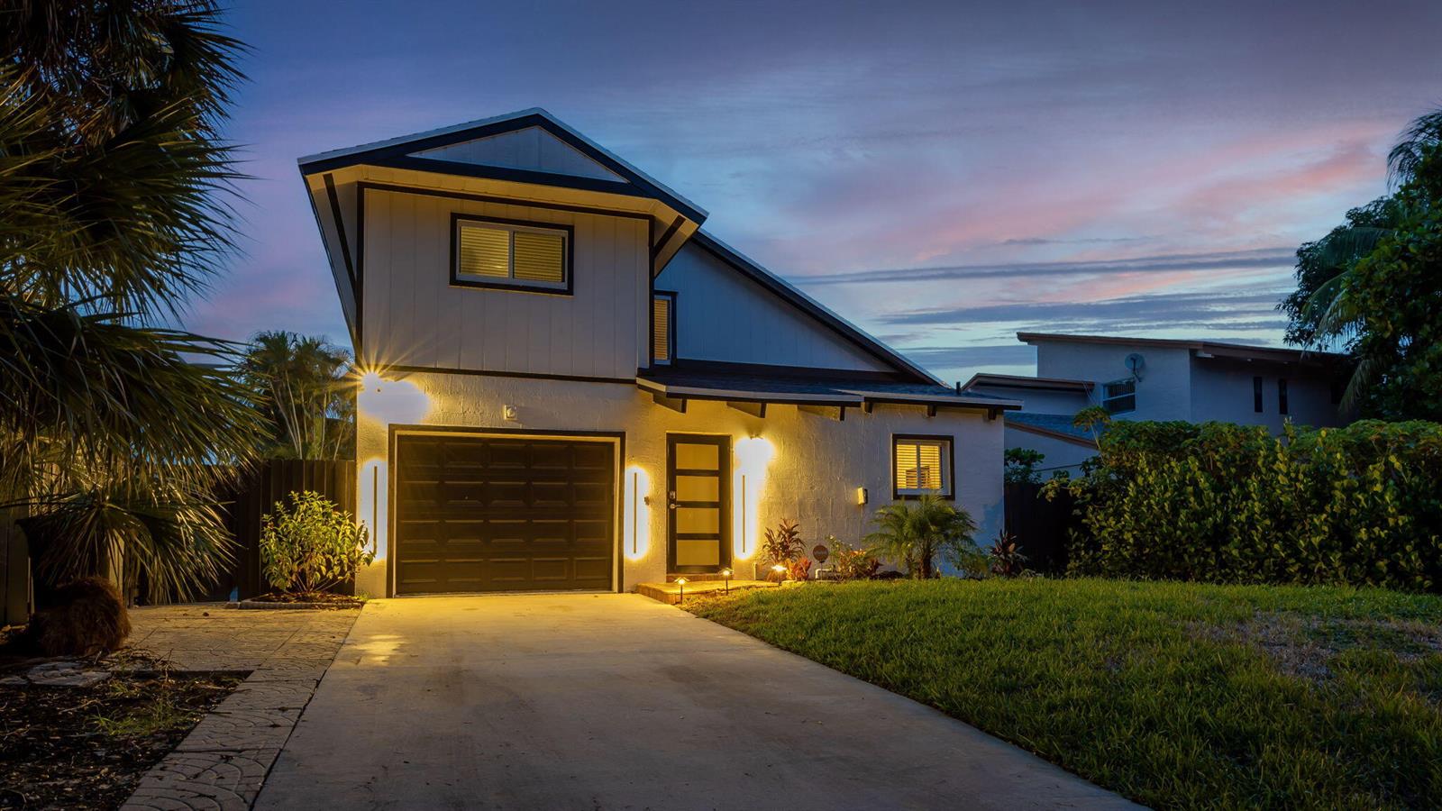 A two-story house with a dark garage door and exterior wall lighting at dusk — 2541 Southridge Road, Delray Beach FL 33444, DELRAY BEACH, FL