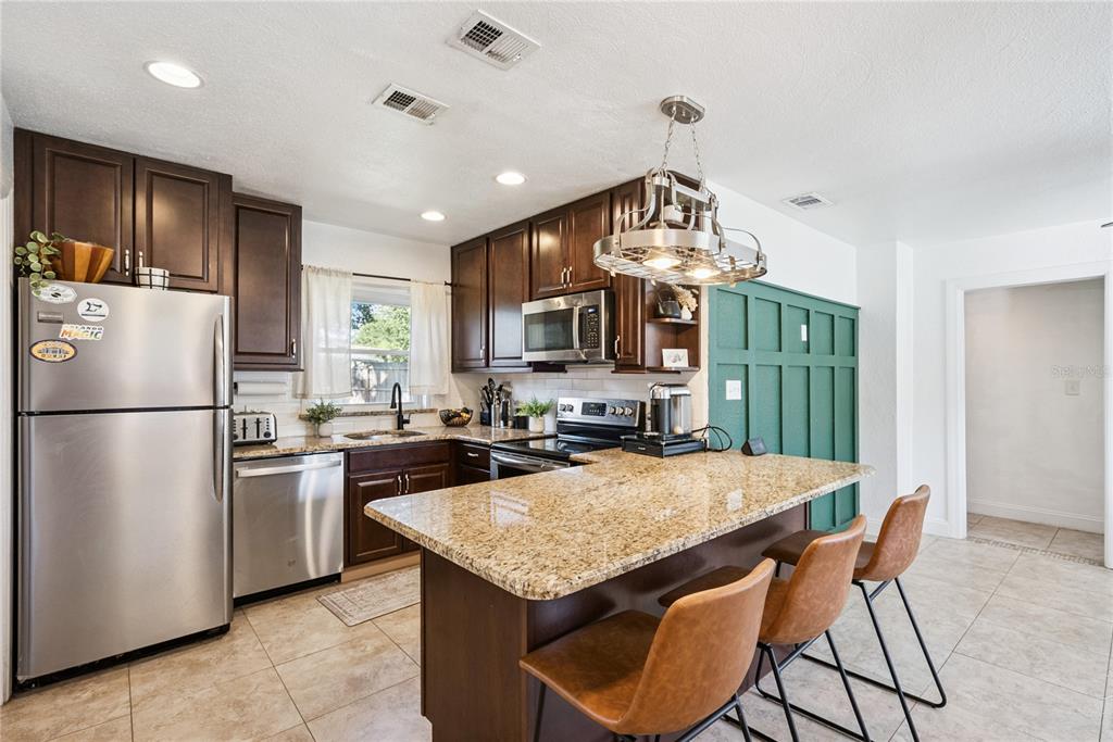 A kitchen features dark wood cabinets, granite countertops, a central island, and green wall paneling — 1909 FERN CIRCLE, ORLANDO, FL