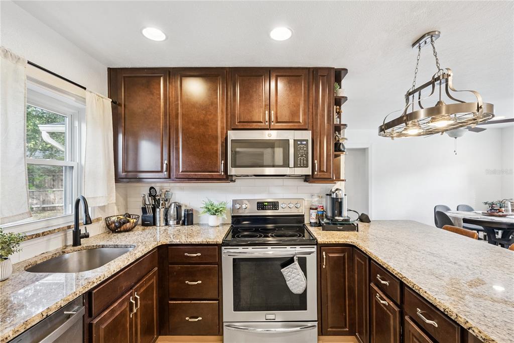 A kitchen features dark wood cabinets, granite countertops, stainless steel appliances, and a hanging light fixture — 1909 FERN CIRCLE, ORLANDO, FL
