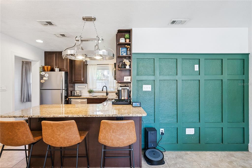 A kitchen features a granite-topped island, dark wood cabinetry, and a green paneled accent wall — 1909 FERN CIRCLE, ORLANDO, FL