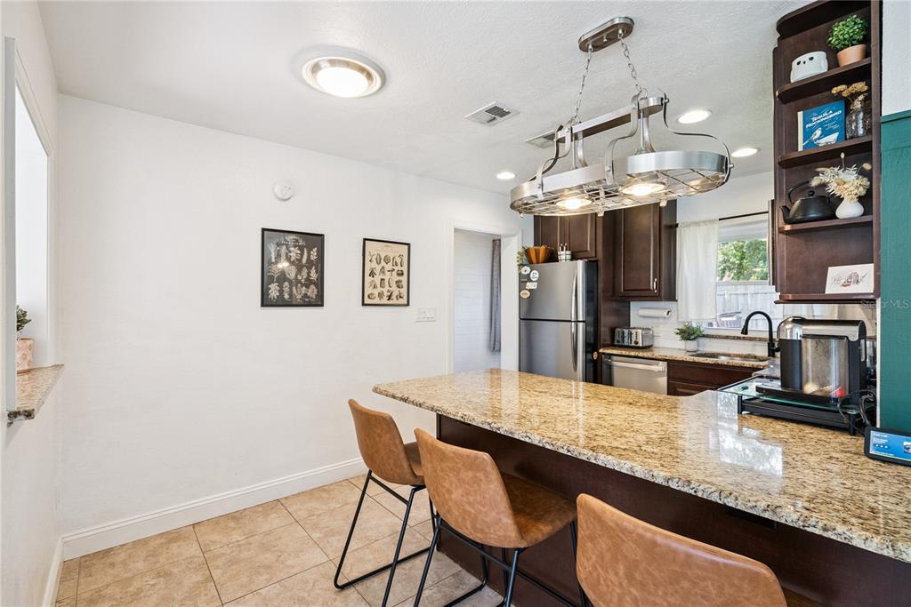 A kitchen features a granite-topped island with three brown stools and dark wood cabinetry — 1909 FERN CIRCLE, ORLANDO, FL