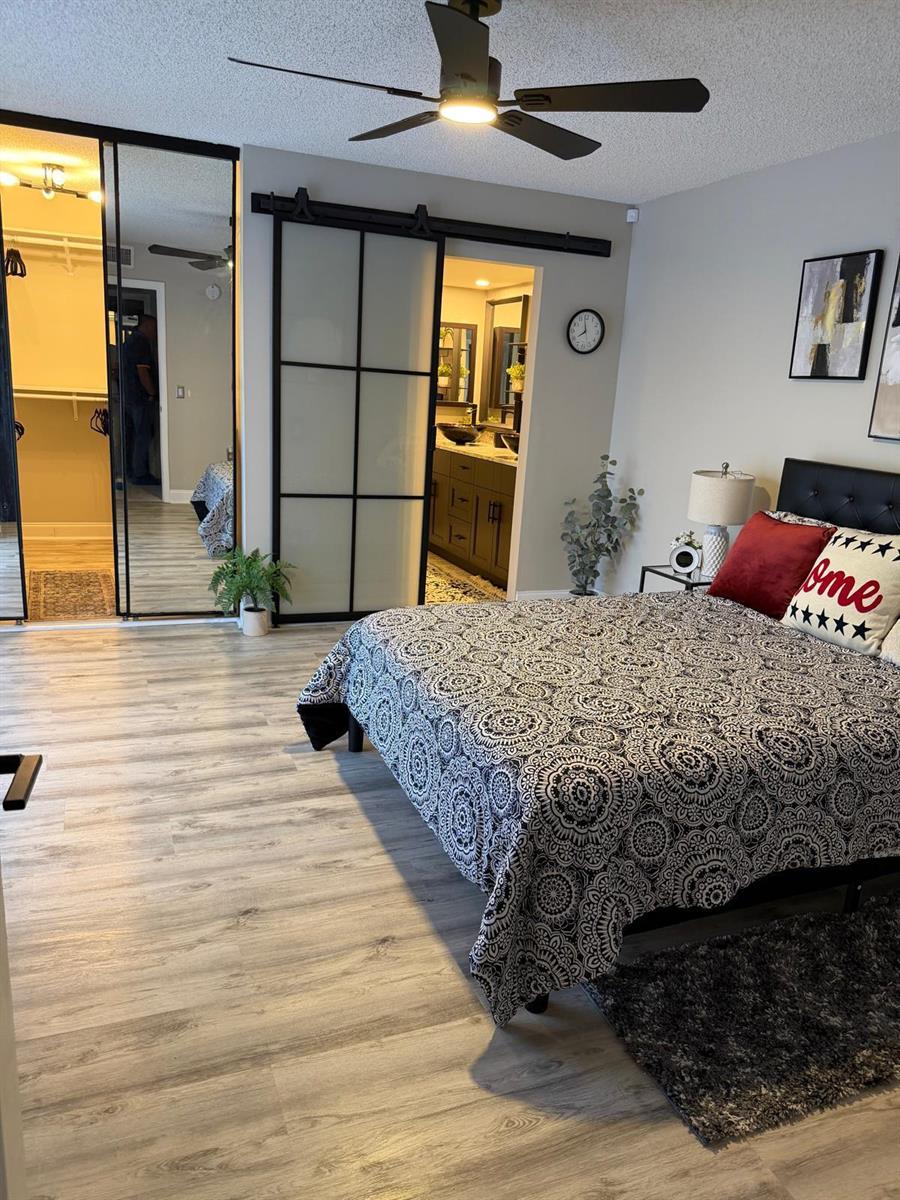 A bedroom features wood-look flooring, a sliding barn door to the bathroom, and mirrored closet doors — 2949 SW 22nd Circle # 27a, Delray Beach FL 33445, DELRAY BEACH, FL