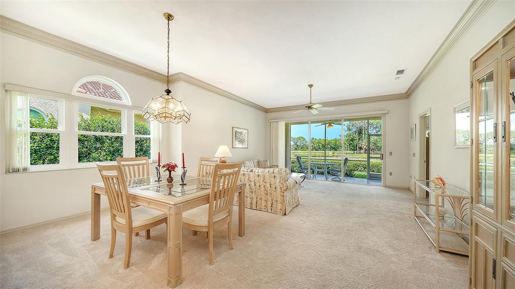 A dining area with a glass-top table and chairs opens to a living room with patio access — 3374 W CHELMSFORD COURT UNIT 9, SARASOTA, FL