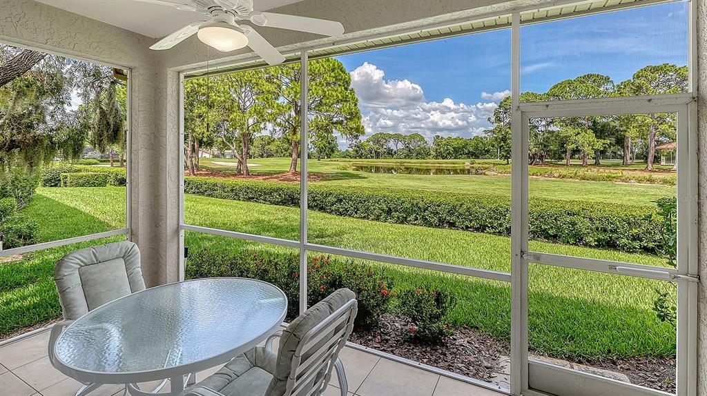 A screened-in patio features a glass table and chairs overlooking a golf course and pond — 3374 W CHELMSFORD COURT UNIT 9, SARASOTA, FL