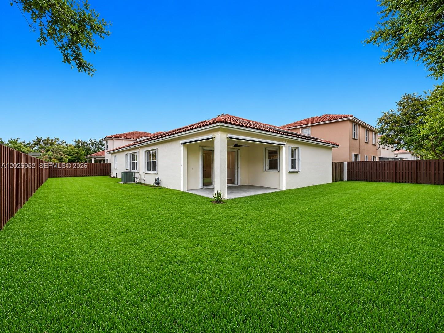 A single-story house with a covered patio and a large fenced backyard under a blue sky — 16204 Opal Creek Dr, Weston FL 33331, WESTON, FL