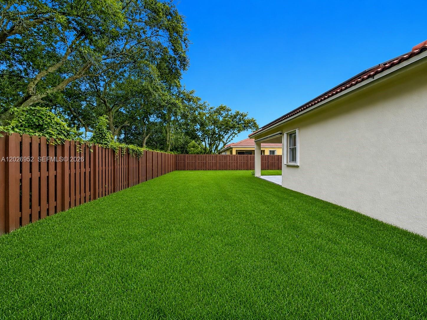 A backyard features a green lawn, a wooden fence, and the side of a house — 16204 Opal Creek Dr, Weston FL 33331, WESTON, FL
