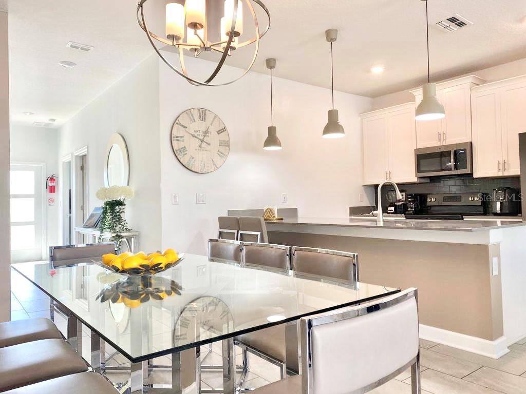 A dining area with a glass table and chairs sits adjacent to a modern kitchen — 8955 CABOT CLIFFS DRIVE, DAVENPORT, FL