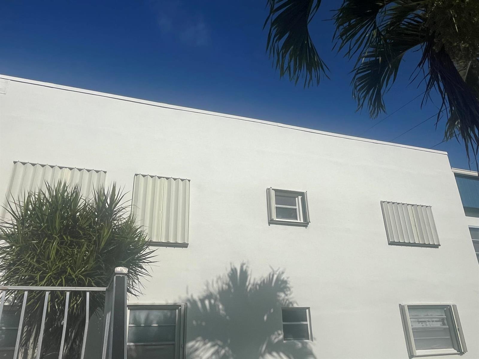 A white exterior wall of a building features several windows with metal hurricane shutters — 526 Normandy K, Delray Beach FL 33484, DELRAY BEACH, FL
