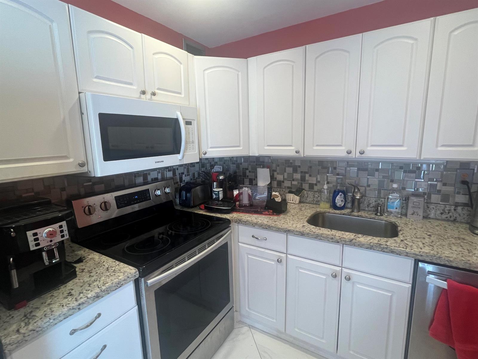 A kitchen features white cabinetry, granite countertops, a stainless steel stove, and a mosaic backsplash — 526 Normandy K, Delray Beach FL 33484, DELRAY BEACH, FL