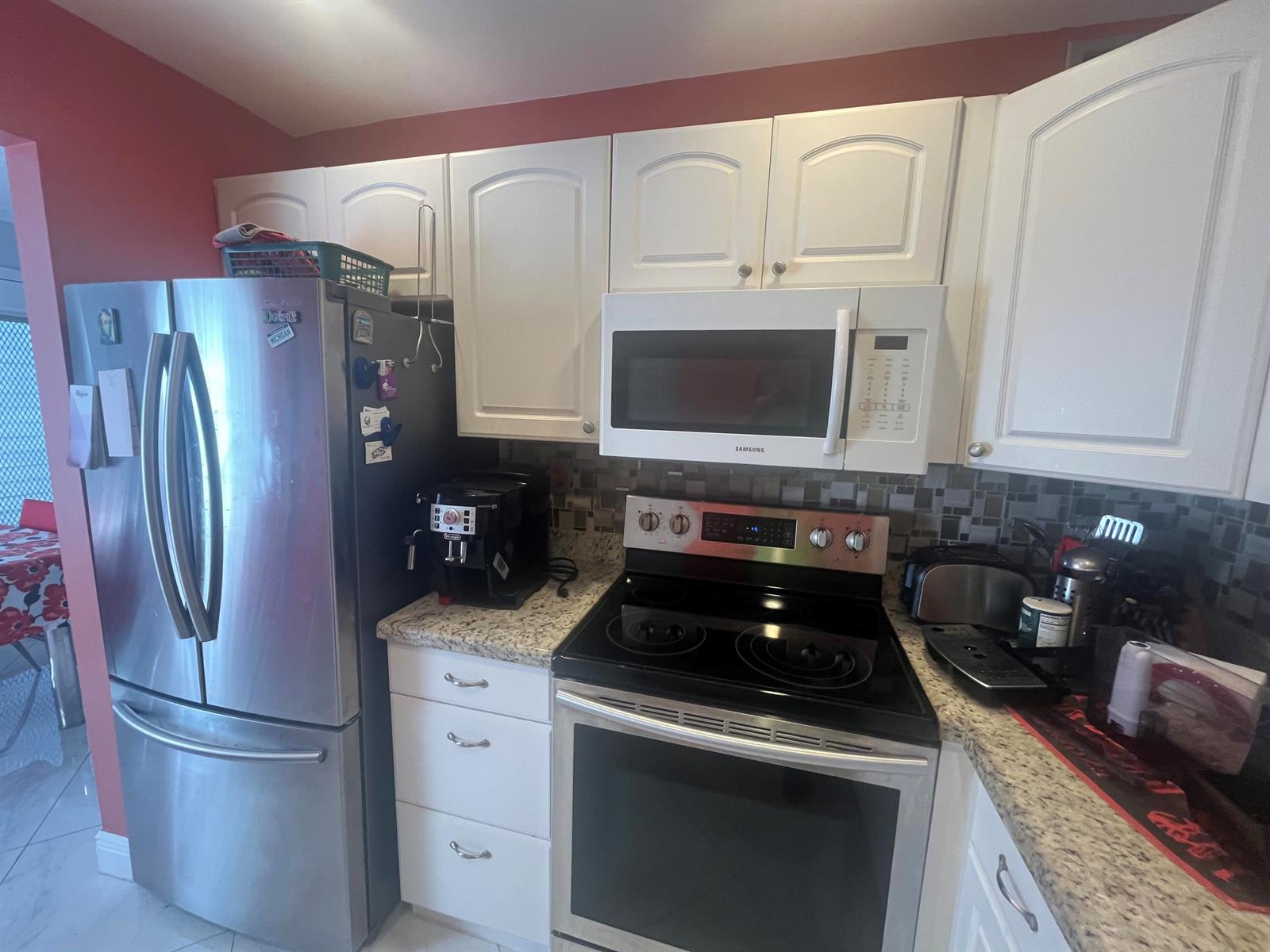 A kitchen features white cabinets, granite countertops, stainless steel appliances, and a mosaic tile backsplash — 526 Normandy K, Delray Beach FL 33484, DELRAY BEACH, FL