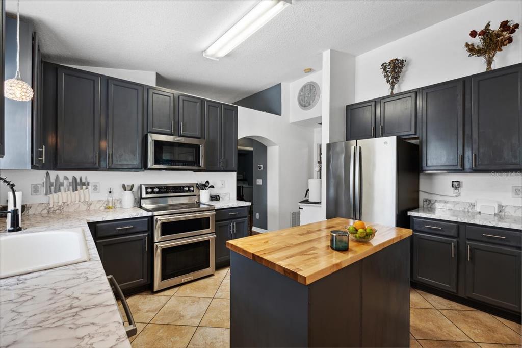A kitchen features dark cabinets, stainless steel appliances, a wood-topped island, and marble-patterned countertops — 24 RIVIERA ESTATES COURT, PALM COAST, FL