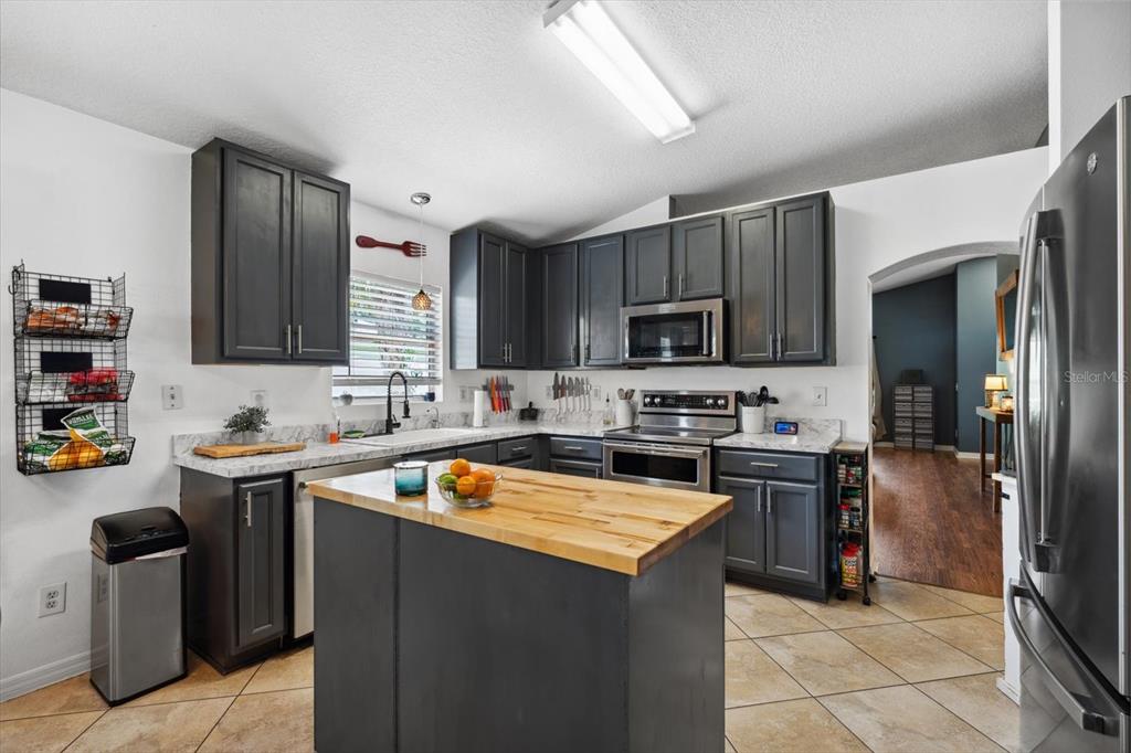 A kitchen features dark gray cabinets, a wooden island countertop, and stainless steel appliances — 24 RIVIERA ESTATES COURT, PALM COAST, FL