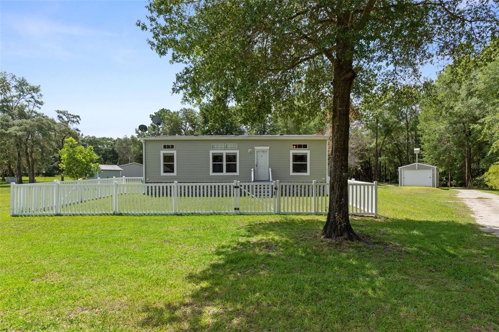 A light green manufactured home sits on a grassy lot behind a white picket fence — 18303 SW 27TH STREET, DUNNELLON, FL