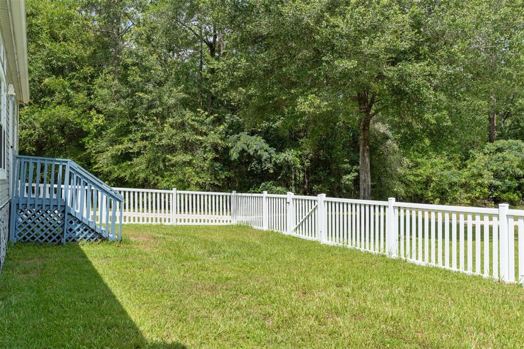 A backyard features a white vinyl fence, a blue wooden deck, and surrounding trees — 18303 SW 27TH STREET, DUNNELLON, FL