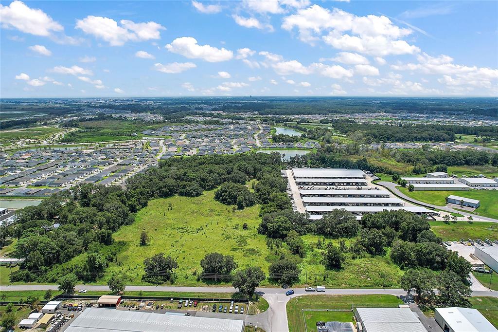 An aerial view shows a large, undeveloped grassy lot bordered by trees, warehouses, and residential neighborhoods — 4609 COUNTY ROAD 156, WILDWOOD, FL