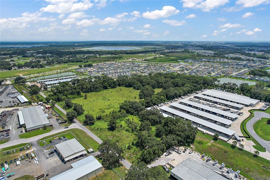 An aerial view shows industrial warehouse buildings, storage lots, and a large residential neighborhood nearby — 4609 COUNTY ROAD 156, WILDWOOD, FL