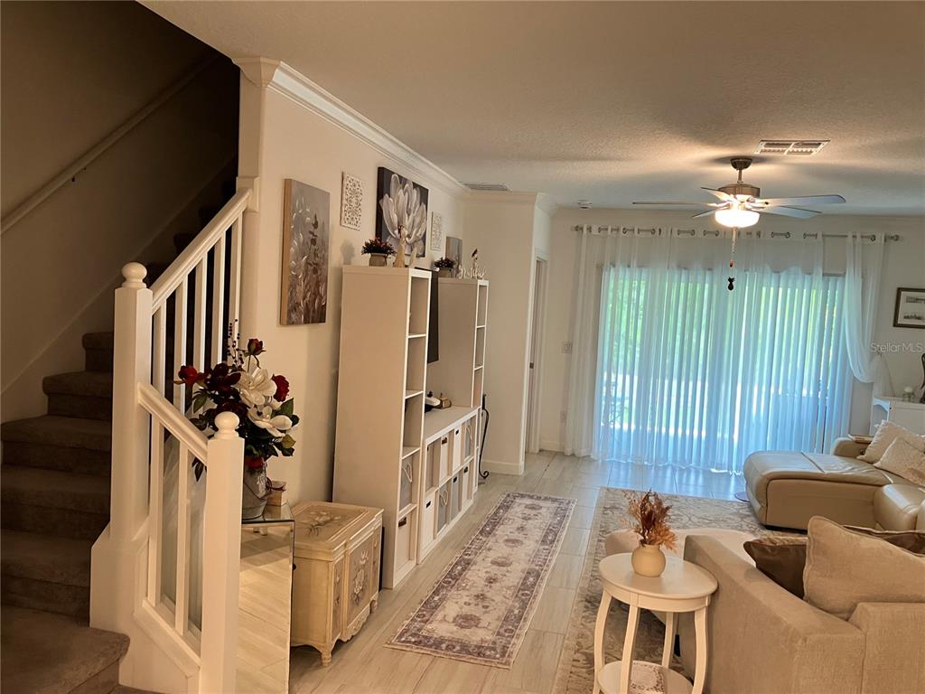 A living room features a staircase, white shelving, tile flooring, and sliding glass patio doors — 16579 SHELL BAY DRIVE, LAND O LAKES, FL