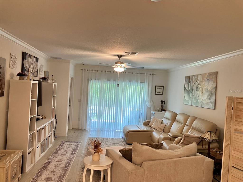 A living room features a beige sectional sofa, a white shelving unit, and tile flooring — 16579 SHELL BAY DRIVE, LAND O LAKES, FL