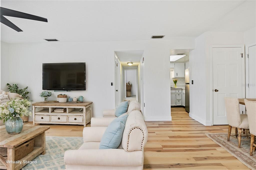 A living room with light wood floors, a television, and a view into the kitchen — 3800 SAXON DRIVE UNIT C52, NEW SMYRNA BEACH, FL