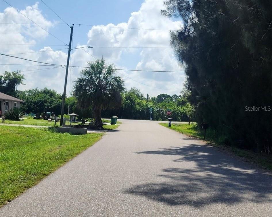 A paved road leads toward a stop sign surrounded by trees and a palm tree — 26532 ANGELICA ROAD, PUNTA GORDA, FL